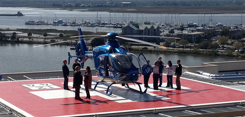 FEC rooftop helipad on building near water, with blue helicopter, flight crew and staff surrounding the helicopter