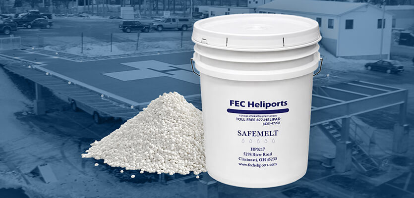 Bucket of FEC Heliports SAFEMELT snowmelt next to a pile of granules, shown in front of a heliport landing pad.